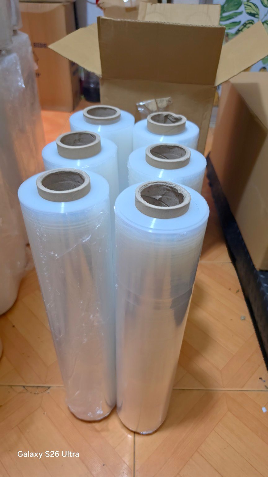 Six clear stretch film rolls standing upright in front of an open carton